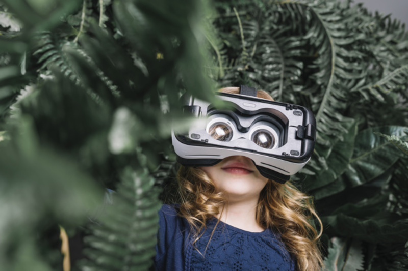 Smiling Blonde Little Girl Using Virtual Headset Standing Among Green Plant 23 2148040059